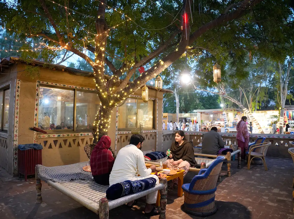 Guests relaxing on traditional charpais under glowing fairy lights during evening at Chaye Dera in Lahore Organic Village
