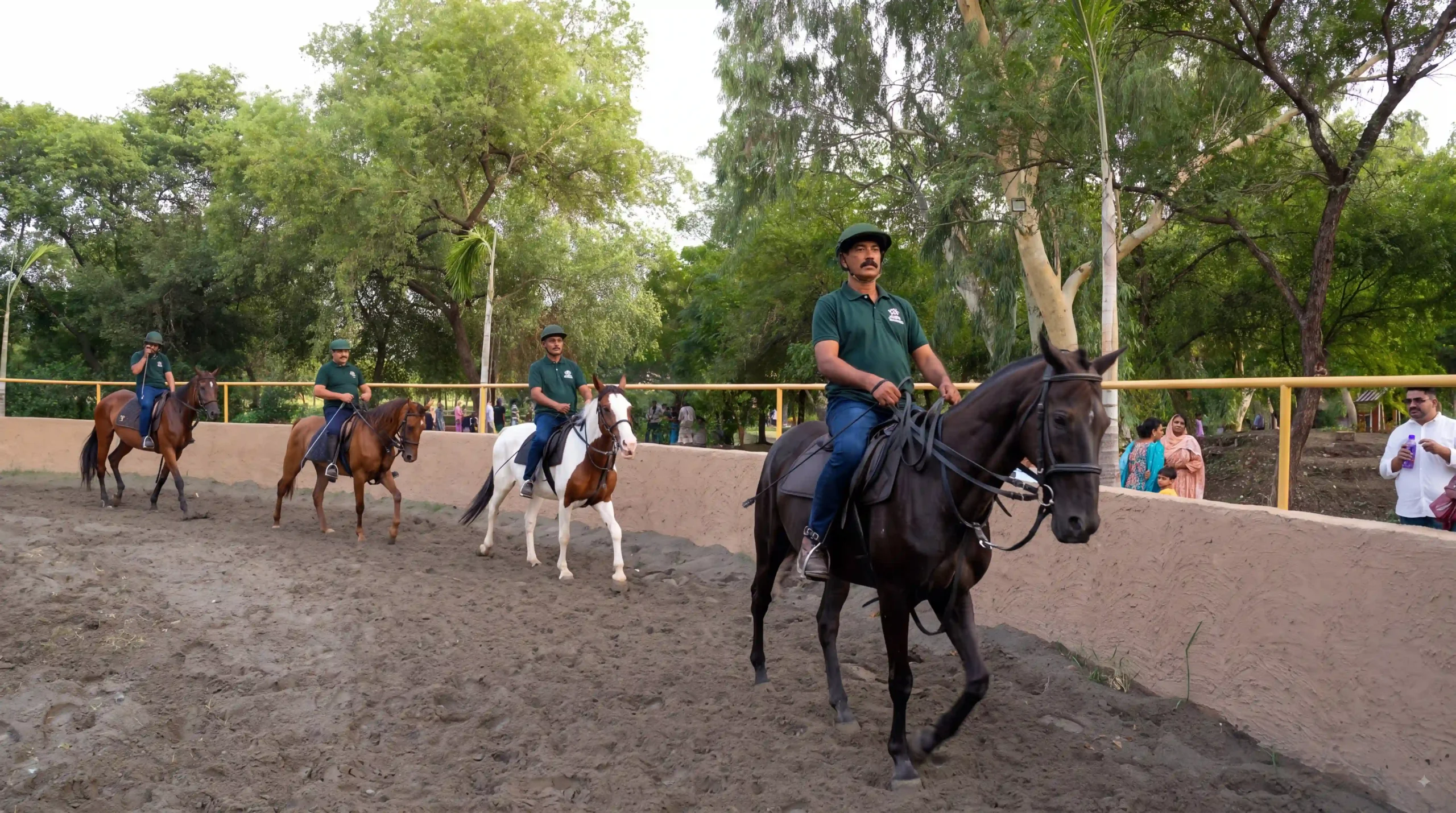 Equestrians riding horses along the dirt track inside Greenwood Horse Riding Arena