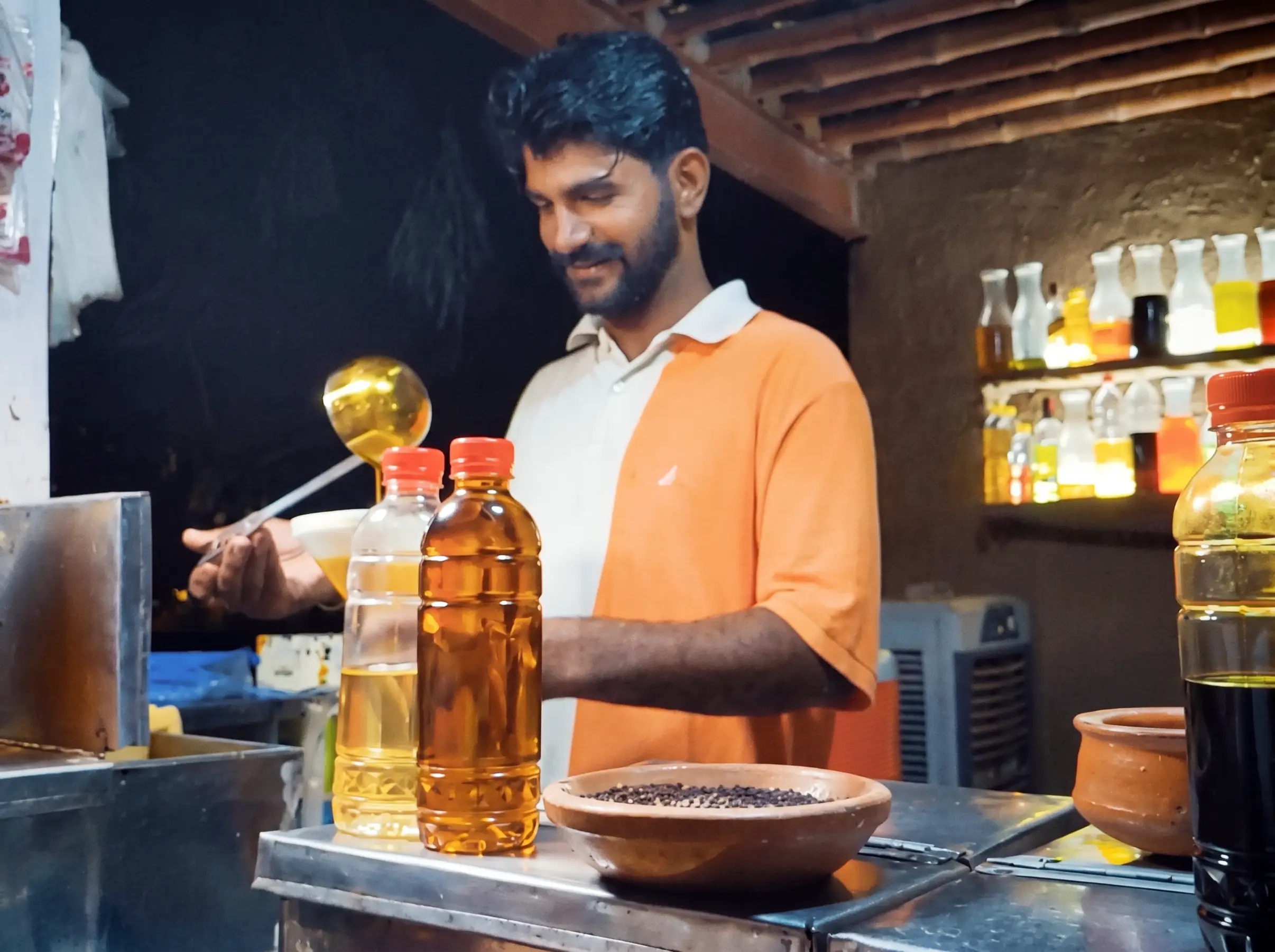 Shopkeeper pouring natural wood-pressed mustard oil into bottles at Fazal Oil Kohlu store, Lahore.